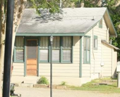Exterior view of Cabin 7 surrounded by trees, featuring a spacious porch and large windows, ideal for family getaways.